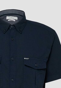 Chemise bleu marine foncé à manches courtes avec col, poche poitrine boutonnée et étiquette "Élégance Décontractée" sur la poche.