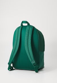 Rucsac verde cu curele umplute, texturate și o bază dintr-un material neted, în contrast. Dispune de o mânere superioară și un design minimalist.