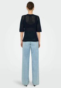 Maglione navy a maniche corte con design a trama aperta, abbinato a jeans azzurri a gamba larga. Texture liscia, taglio casual.