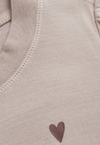 Beige trui stof met een zachte textuur, voorzien van een klein bruin hartje geborduurd nabij de onderkant. Ronde halslijn en gestikte details.
