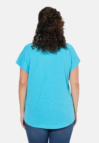 Camiseta de manga corta en color turquesa con un corte holgado, escote redondo y dobladillo curvado, fabricada con una tela liviana y texturizada.