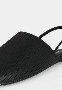 Μαύρο μπαλαρίνα με μυτερή μύτη, υφή στην επάνω επιφάνεια και στενή ελαστική λουρίδα στη φτέρνα σε λευκό φόντο.