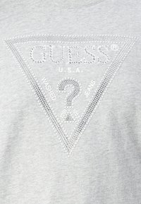 Grå sweatshirt med et trekantet rhinestones-mønster og teksten "GUESS U.S.A." og "WASHED JEANS" i en kontrasterende skrift.