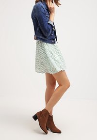 Jeansjacka med långa ärmar över en grön mönstrad skaterklänning. Bruna mockaankelboots med klack.