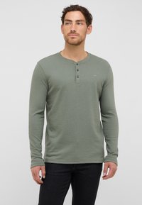 Koszula henley z długim rękawem w kolorze szałwii, wykonana z teksturowanej tkaniny, z trzykrotnym zapięciem na guziki i subtelnym logo na klatce piersiowej.