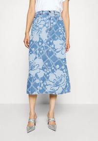 Falda midi de mezclilla con un patrón floral en tonos de azul claro, corte recto y botones en el frente. Combinada con tacones plateados de punta afilada.