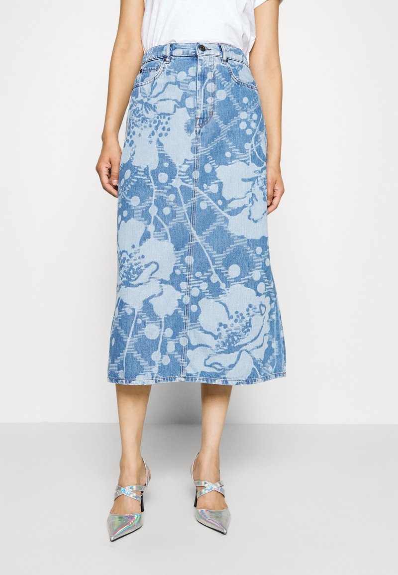 Falda midi de mezclilla con un patrón floral en tonos de azul claro, corte recto y botones en el frente. Combinada con tacones plateados de punta afilada.