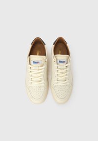 Ténis de cor creme com detalhes perfurados, atacadores planos e interior em pele castanha. Apresentam um pequeno logótipo multicolorido na língua.