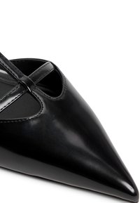 Scarpa nera a punta in pelle lucida con dettagli intagliati e sottili cinturini. Tessuto liscio e design snello.