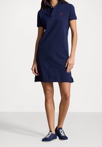 Námořnické polo šaty vyrobené z bavlny, s límečkem, krátkým rukávem, bočními rozparky a malým červeným logem na hrudi. V kombinaci s námořnickými teniskami.