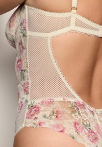 Kermaruinen pitsivartalo, jossa on kukkakuvioita, käytetään henkilöllä. Siinä on verkko-osia ja säädettävät olkaimet.