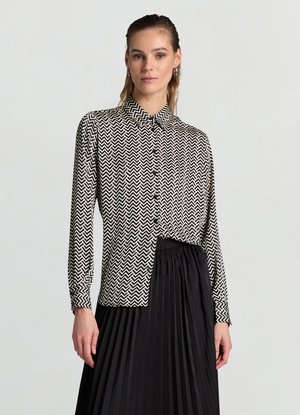 Camicia in bianco e nero con motivo a chevron, colletto, maniche lunghe e chiusura con bottoni, abbinata a una gonna nera plissettata.
