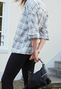 Chemise à carreaux bleu clair et blanc à boutons avec manches retroussées, associée à des leggings noirs et un petit sac à main noir. Tenue décontractée.