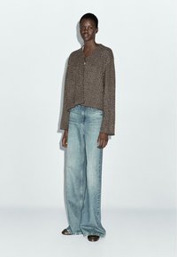 Gebreide cardigan in bruin met verticale strepen, voorzien van een ronde halslijn en knoopsluiting, gecombineerd met lichtblauwe wijde jeans.