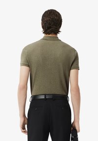 Polo de color verde oliva con tejido texturizado, mangas cortas y cuello doblado, combinado con pantalones negros y un cinturón negro.