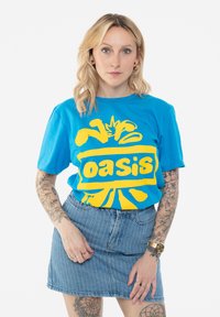 Blue cotton t-shirt with yellow "Oasis" graphic. Short sleeves, relaxed fit. Paired with a light blue denim skirt with vertical stripes.