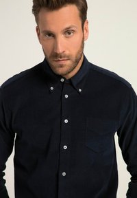 Camisa azul marino de botones fabricada en tejido texturizado, con un bolsillo en el pecho y acentos en botones blancos. Diseño clásico de cuello.
