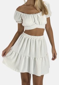 Witte tweedelige outfit met een cropped top met pofmouwen en een wijde, gelaagde rok. De stof heeft een zachte, gestructureerde afwerking.