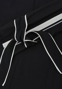 Melna auduma ar baltām svītrām un mezglotu jostas detaļu. Materiāls izskatās gluds un nedaudz strukturēts.