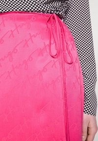 Růžová sukně s texturovaným povrchem a opakovaným logem "Hugo", spárovaná s černo-bílým kostkovaným topem s dlouhým rukávem.