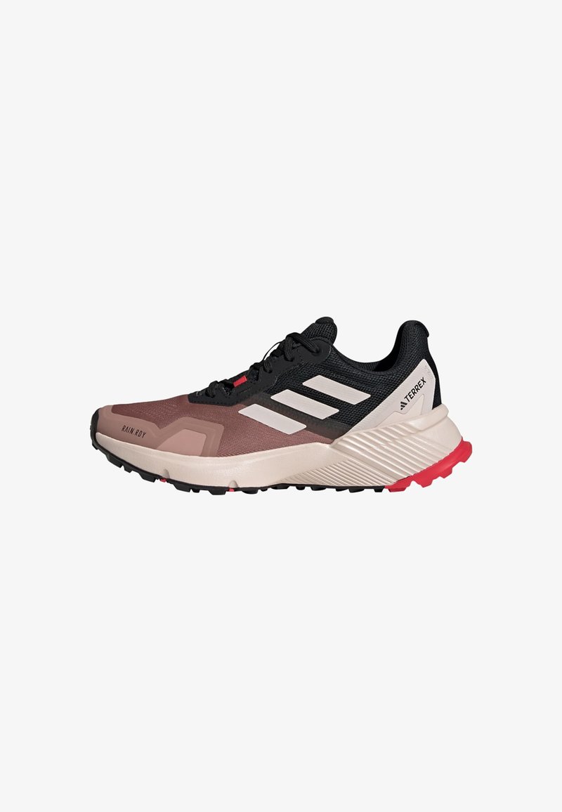 Running shoes with a black and brown mesh upper, white stripes, cushioned beige midsole, and red accents on the outsole.