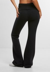 Black, flared knit pants with a ribbed high waistband and a smooth texture, featuring a relaxed fit down to the ankles.