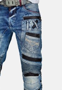 Pantaloni cargo in denim blu chiaro. Presentano più tasche, dettagli in pelle nera e motivi cuciti. Dettagli testurizzati lungo le gambe.