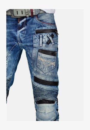 Pantaloni cargo in denim blu chiaro. Presentano più tasche, dettagli in pelle nera e motivi cuciti. Dettagli testurizzati lungo le gambe.