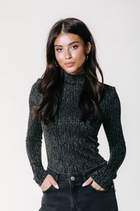 Cămașă neagră cu mânecă lungă, cu guler înalt, având un model texturat cu dungi verticale argintii, purtată împreună cu pantaloni negri cu talie înaltă.