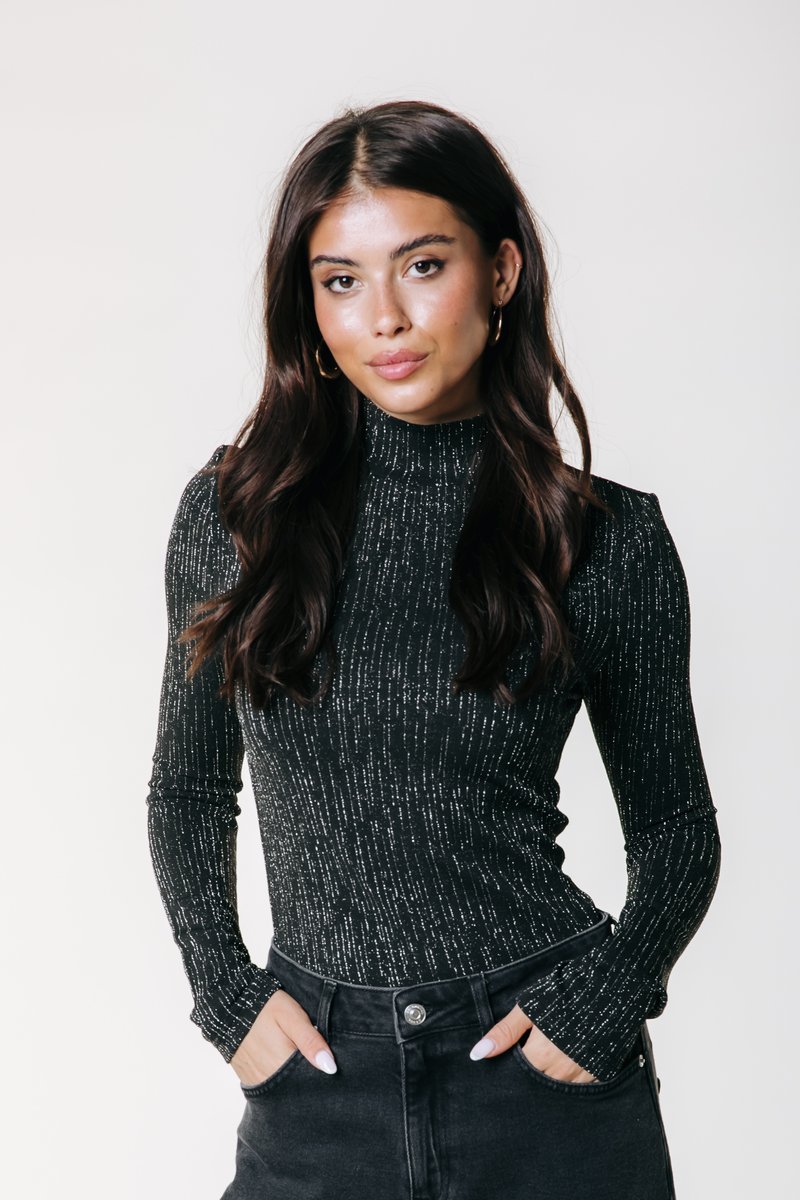 Cămașă neagră cu mânecă lungă, cu guler înalt, având un model texturat cu dungi verticale argintii, purtată împreună cu pantaloni negri cu talie înaltă.