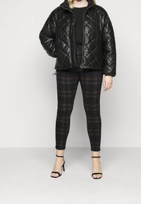 Mustat tilkkuvuoratut puffer-takit korkealla kauluksella, käytetty mustan paidan päällä, yhdistetty musta-punaisiin ruudullisiin legginsseihin ja mustiin korkokenkiin.