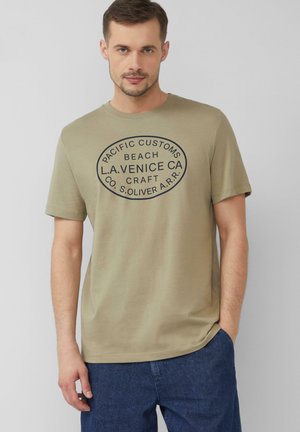 Kahakifarbenes Baumwoll-T-Shirt mit kurzen Ärmeln, das einen runden dunkelblauen Druck mit Text zeigt. Rundhals-Ausschnitt und entspannte Passform.