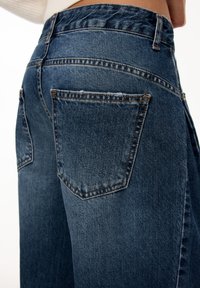 Dark blue denim jeans with a high waist, featuring two back pockets and stitch detailing. The fabric has a slightly textured appearance.