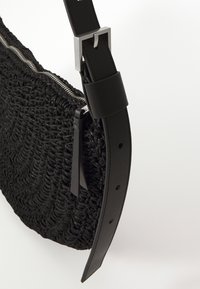 Borsa a tracolla nera tessuta con superficie testurizzata, dotata di una cerniera in tono argento e di una robusta tracolla in pelle con fibbia metallica.