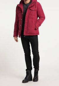 Rød puffjakke med hætte, har to brystlommer, sidelommer og en lynlås. Bæres over en sort skjorte og parret med sorte bukser og støvler.