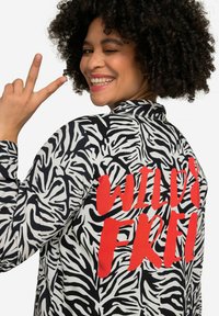 Schwarz-weiße Jacke im Zebra-Muster mit rotem "WILD & FREE"-Text. Mit hohem Kragen und langen Ärmeln mit Manschettendetails.