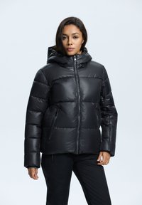 Chaqueta de plumas negra con capucha, con cierre de cremallera frontal, puños elásticos y dos bolsillos laterales con cremallera. Acabado liso y brillante con secciones acolchadas.