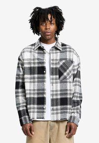 Chemise en flanelle à carreaux noir et blanc dotée d'un col, d'une fermeture par boutons, d'une poche poitrine et d'une coupe décontractée. Tissu doux avec des textures variées.