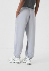 Pantaloni della tuta grigi chiari con vita elasticizzata, polsini affusolati e tasche laterali, abbinati a sneaker bianche con dettagli argento.