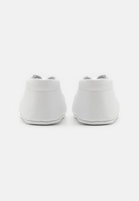 Weiße Kunstleder-Schuhe mit glatter Textur, abgerundetem Silhouette und minimalistischem Design, mit gesteppten Details auf der Sohle.