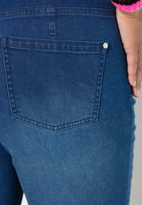 Tmavě modré džíny s viditelnou zadní kapsou. Kapsa má stříbrné cvoky a jemné vyblednutí látky.