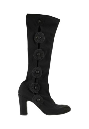 Botte noire à talon haut mi-mollet avec cinq boutons décoratifs noirs en forme de fleur le long du côté extérieur et un bout arrondi.