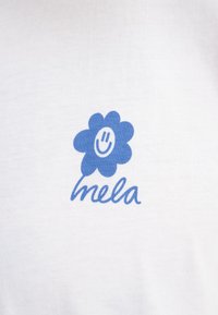 Witte katoenen t-shirt met een blauwe bloemenafbeelding met een glimlachend gezicht. Daaronder staat het woord "mela" in cursieve letters.