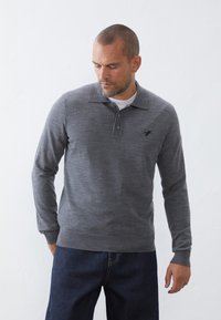 Grå langærmet polo med en subtil tekstur, der har en tre-knaps placket og et broderet logo på brystet. Bæret med mørk denim.