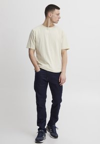 Camiseta de algodón beige, de manga corta; vaqueros de mezclilla azul oscuro, de corte recto; zapatillas deportivas negras y marinas con acentos blancos.