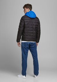 Zwarte gewatteerde jas met een felblauwe capuchon, met horizontaal gestikte secties, gecombineerd met blauwe jeans en witte sneakers.