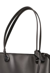 Zwarte leren totebag met twee lange handvatten, een gladde textuur en een eenvoudig ontwerp. Voorzien van een ronde metalen decoratie en een geknoopt detail.