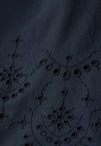 Tessuto blu navy con un ricamo intricato che presenta motivi floreali e fori ritagliati. Il design mette in evidenza un aspetto testurizzato e stratificato.