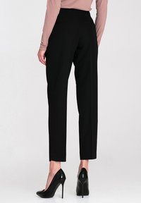 Czarne dopasowane spodnie z wysokim stanem, prostym krojem i minimalistycznymi kieszeniami z tyłu, w połączeniu z czarnymi szpilkami.