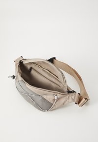 Tan sling bag with a mesh panel, zippered main compartment, inner pocket, adjustable strap, and a smooth textured surface.